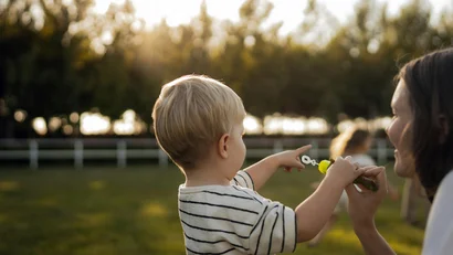 Bambino che indica qualcosa mentre tiene una bolla di sapone con un adulto in un parco