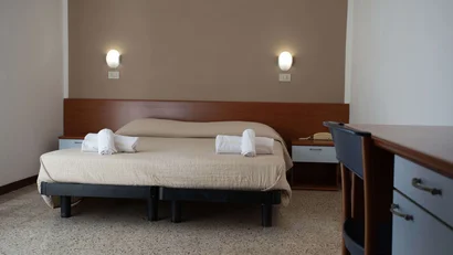 Camera doppia semplice con letto, asciugamani arrotolati, scrivania e lampade da parete