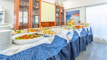 Buffet con piatti di insalate, verdure e cibo in una sala luminosa con armadio e tende