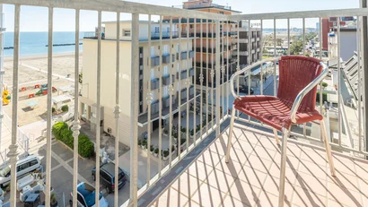 Sedia rossa sul balcone con vista sul mare e edifici circostanti in una giornata soleggiata