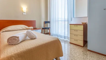 Camera singola con letto, asciugamani arrotolati, sedia e armadio vicino alla finestra