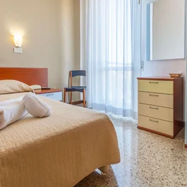 Camera singola con letto, asciugamani arrotolati, sedia e armadio vicino alla finestra