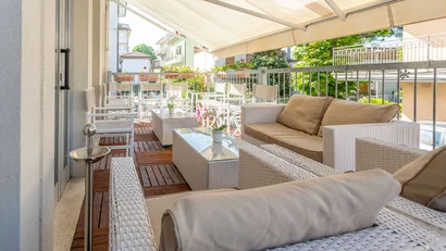 Terrazza con mobili da esterno in vimini bianco e cuscini beige sotto una tenda da sole