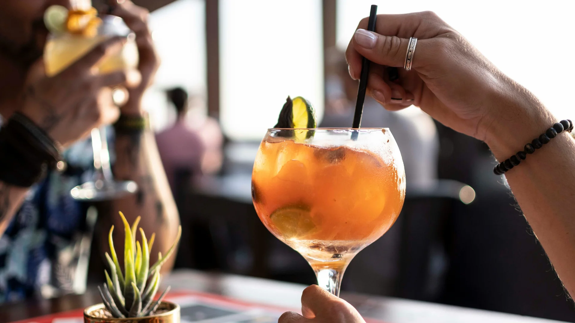 Persona che tiene un bicchiere di cocktail arancione con ghiaccio e lime a un bar