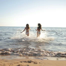 Due ragazze che corrono e schizzano acqua nel mare al tramonto
