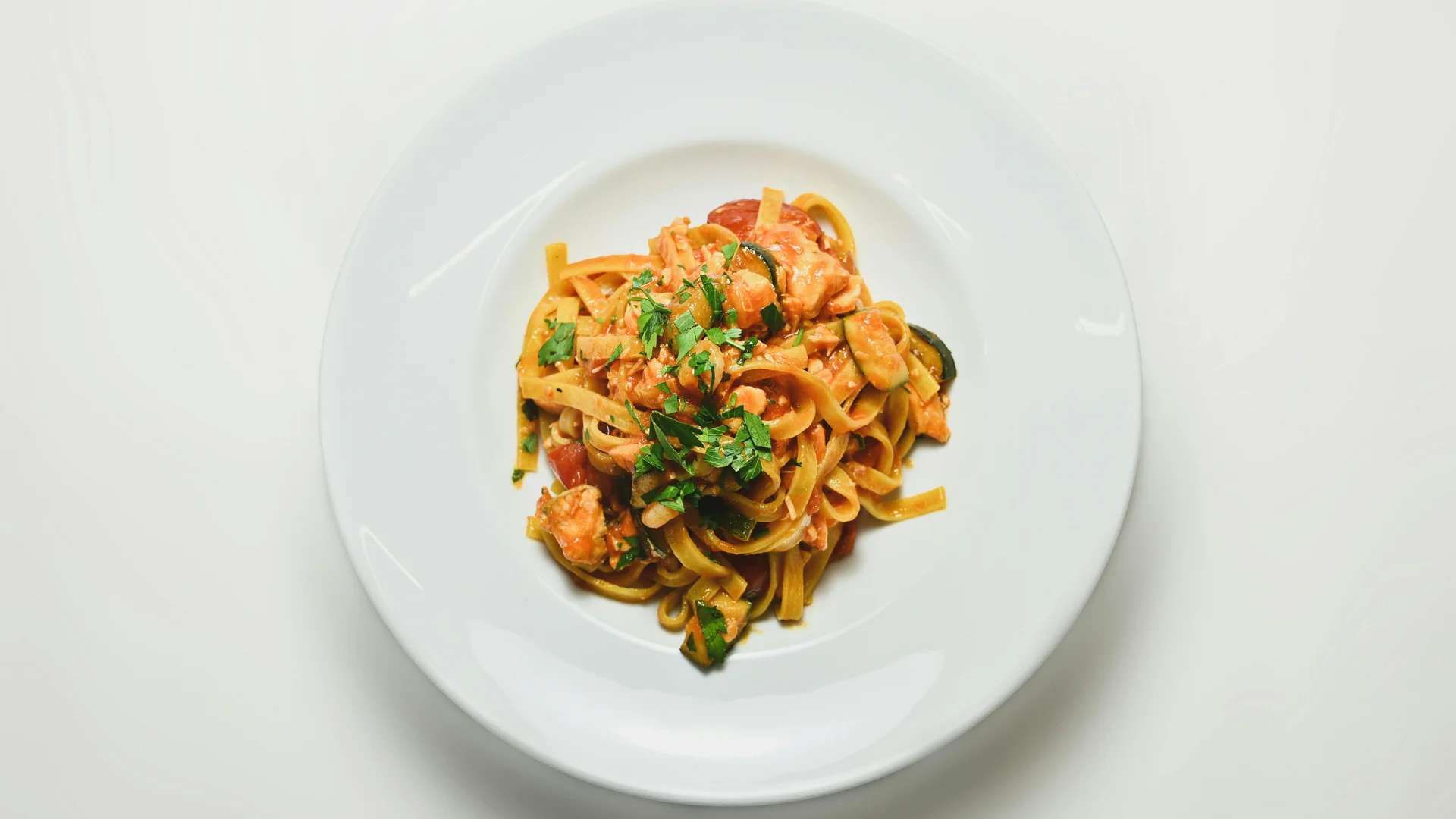 Piatto di pasta con pomodorini, zucchine e prezzemolo su piatto bianco